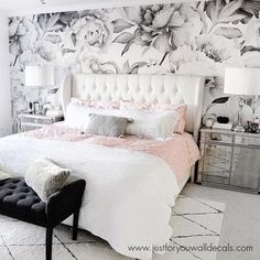 a white bed sitting in a bedroom next to a window with flowers on the wall