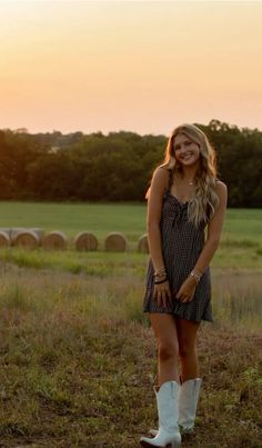 a woman standing in the middle of a field wearing white cowboy boots and a dress