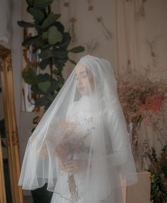 a woman wearing a veil and holding a bouquet in front of a mirror with greenery behind her