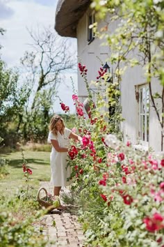 a woman standing in front of a house with flowers on the outside and pink roses growing all around her