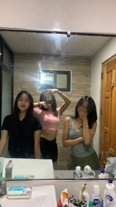 three women standing in front of a bathroom mirror