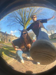 two women are sitting on the ground in front of a tire and one is holding her arms out