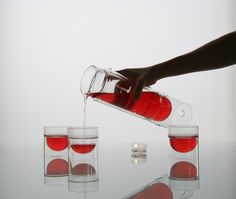 a person pouring red liquid into four glasses