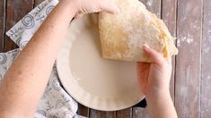 a person holding a piece of bread on top of a white plate next to a wooden table