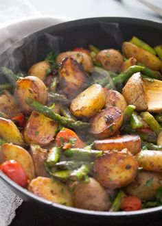 a pan filled with potatoes and asparagus on top of a table next to a napkin