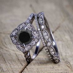 two wedding rings with black and white diamonds in them on top of a piece of wood