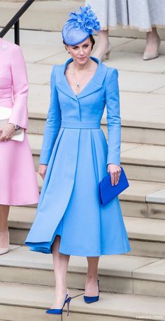 a woman in a blue dress and hat is standing on the steps with her purse