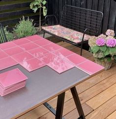 a table with pink tiles on it and some flowers in the back ground next to a bench