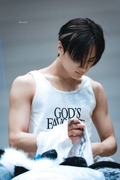 a young man is looking at his cell phone while wearing a tank top that says god's favorite