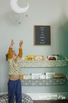 a young boy reaching up to catch a toy in the air with his hands while standing on top of a bed