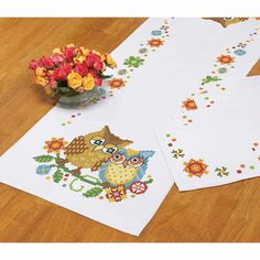 two cross - stitch placemats with an owl and flower arrangement on the table