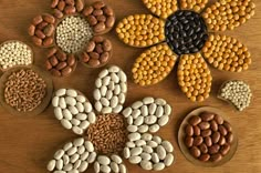 several different types of beans and nuts in bowls on a wooden table with one flower surrounded by smaller ones