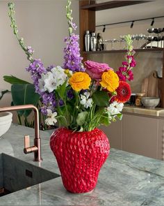 a red vase filled with lots of flowers on top of a counter next to a sink