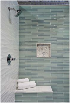 a tiled shower with white towels on the shelf and blue glass tile wall behind it