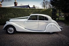 an old white car parked in front of a hedge