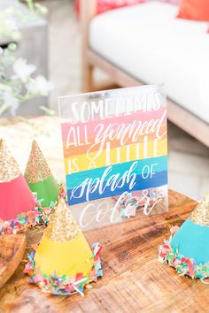 colorful party hats with confetti around them on a wooden table next to a sign that says something all you need is a splash of color