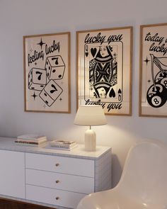 two framed pictures hang on the wall above a dresser in a room with white furniture