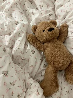 a brown teddy bear laying on top of a white comforter covered in floral sheets