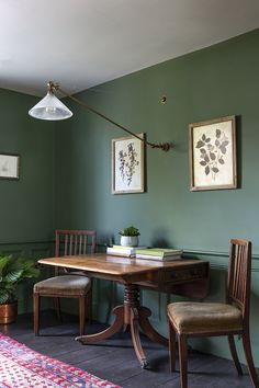 a dining room with green walls and wooden table, two chairs and a rug on the floor