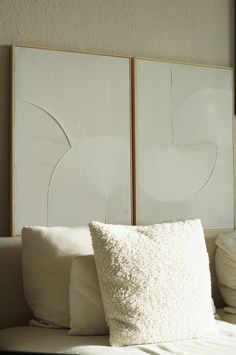 two white pillows sitting on top of a bed next to a wall mounted art piece