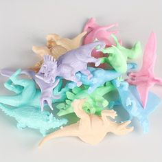 small plastic toy dinosaurs sitting next to each other on a white surface with blue, green, pink and yellow colors