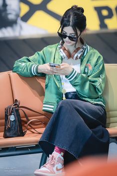 a woman sitting on a bench looking at her cell phone while wearing sunglasses and a green jacket