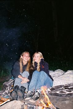 two women sitting next to each other near a campfire