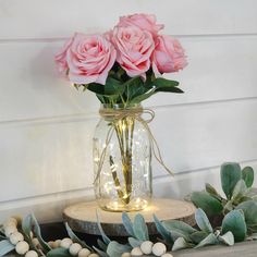 some pink roses are in a mason jar on a wood slab with greenery and lights