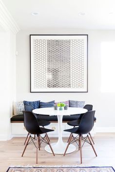 a white table with four black chairs and a painting hanging on the wall above it