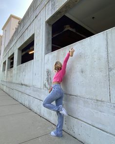 a woman leaning against the side of a building with her hand up in the air