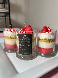 three small desserts with strawberries and whipped cream in them on a white tray