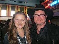 a man in a cowboy hat standing next to a woman wearing glasses and a black shirt