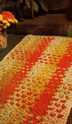 a crocheted blanket with red, yellow and white stripes next to a basket of flowers