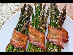 asparagus wrapped in bacon on a white plate with sesame seeds and seasoning