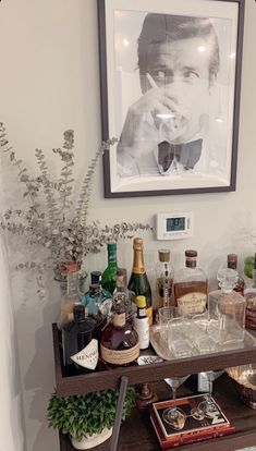 a bar cart with liquor bottles and glasses on it in front of a framed photo