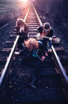 three young children sitting on train tracks with guitars in their hands as the sun goes down