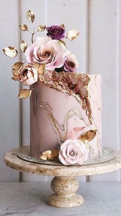 a pink cake with gold leaf and flowers on top is sitting on a small stand