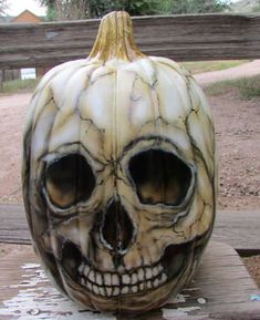 a pumpkin with a skull face painted on it's side sitting on a wooden bench