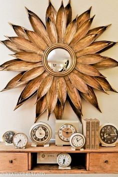 a wooden table topped with clocks and a gold sunburst wall hanging above it