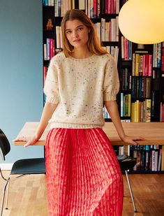 a woman standing in front of a bookshelf wearing a red pleated skirt