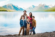 a family poses for a photo in front of a lake with mountains in the background