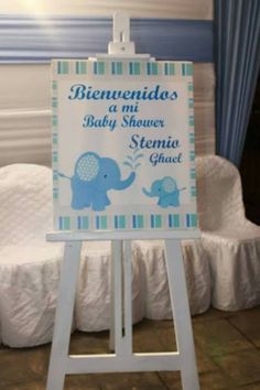 a baby shower sign sitting on top of a wooden easel in front of a bed