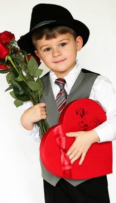 a young boy holding a heart shaped box with roses in it and wearing a hat