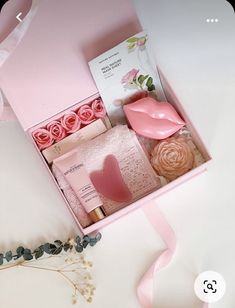 a pink gift box filled with lots of different items next to a ribbon and flowers