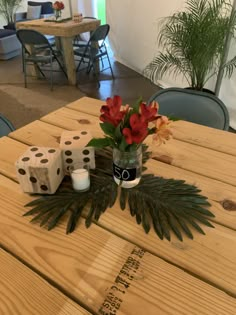 a wooden table with dice and flowers on it in the middle of a room filled with chairs