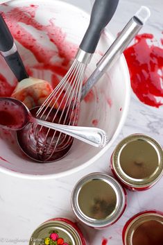 a white bowl filled with red liquid and whisk attachments next to four empty canisters