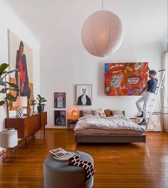 a man standing in the middle of a room with a large bed and artwork on the wall