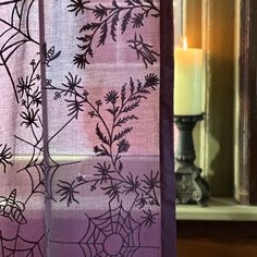 a candle is lit next to a window with spider webs and flowers on it