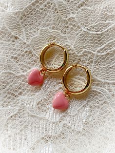 These adorably sweet huggie hoops have a charm of a small puff heart coated in shiny enamel. Huggie style hoop earrings are hinged at the bottom and click to clasp. Choose from pink or white. Gold plated. 7/8" long.