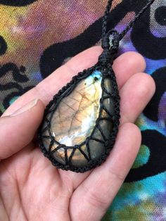 a hand holding a necklace with a tear shaped stone in it's center, on a colorful background